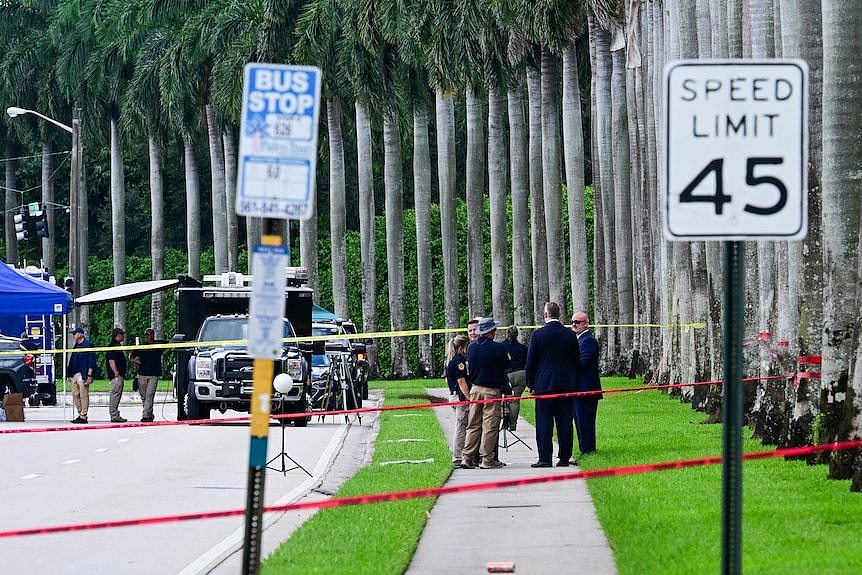 Police talk in a group near a row of palm trees 