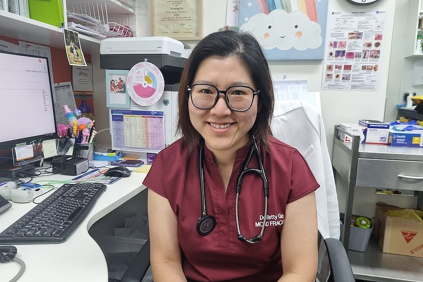 A portrait of a doctor wearing a stethoscope around her neck, seated next to a desk.