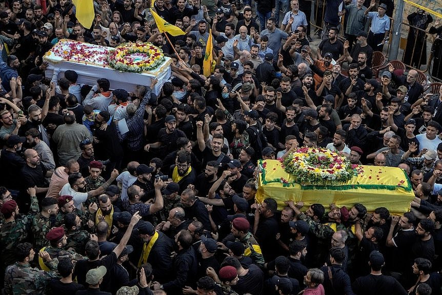 Hundreds of people carry two coffins in a large crowd of people 