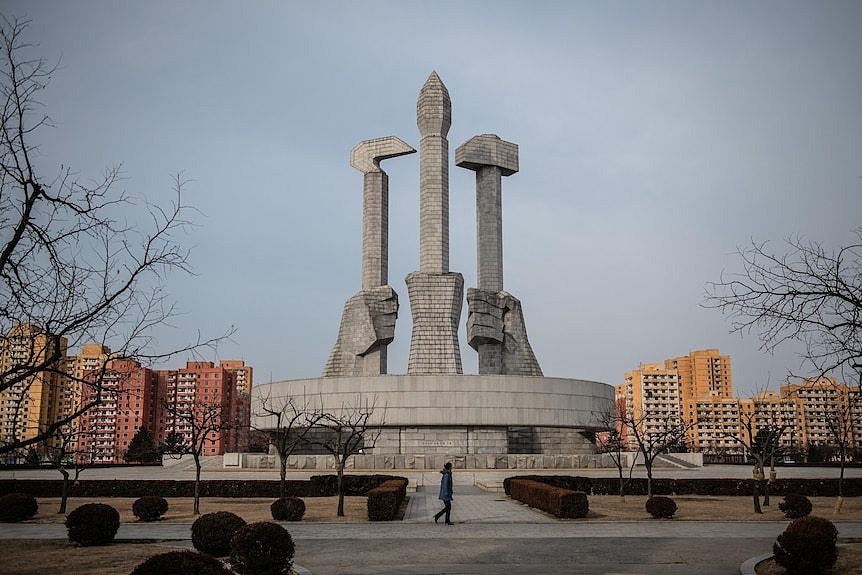 A huge stone monument of three hands holding a hammer, a sickle and a brush