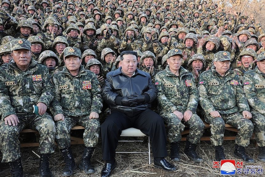 Kim Jong Un sitting among dozens of soldiers, many of whom are cheering.