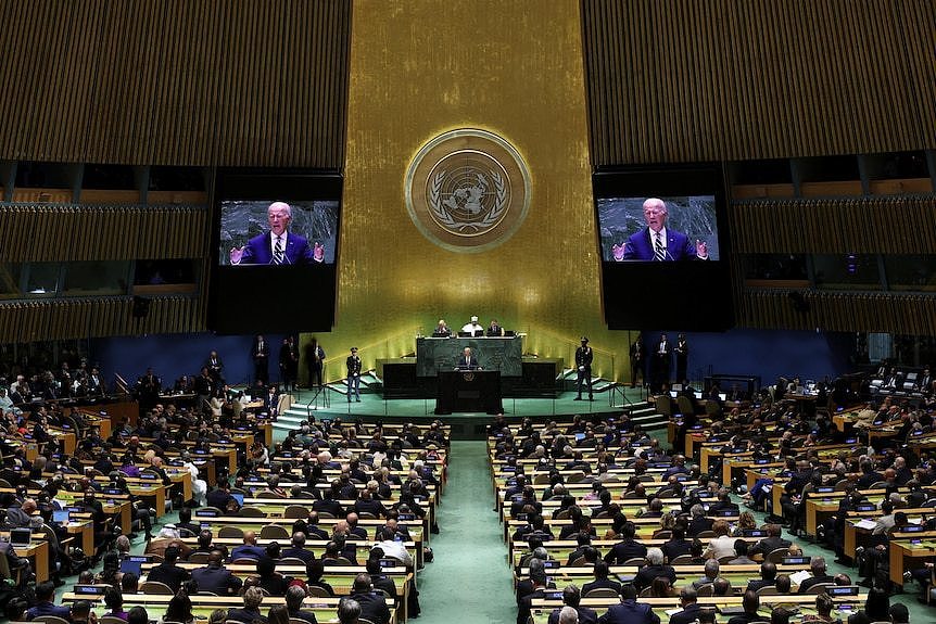 Joe Biden stands at the UN podium and speaks, with large screens behind him. An audience is in front of him.