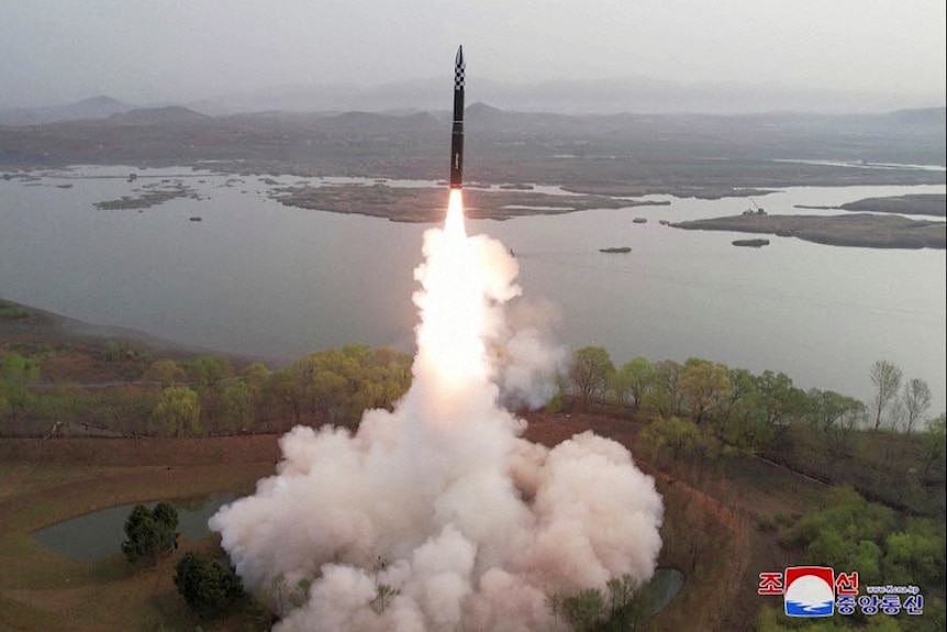 A view of smoke and fire coming from a missle launching in front of a body of water.