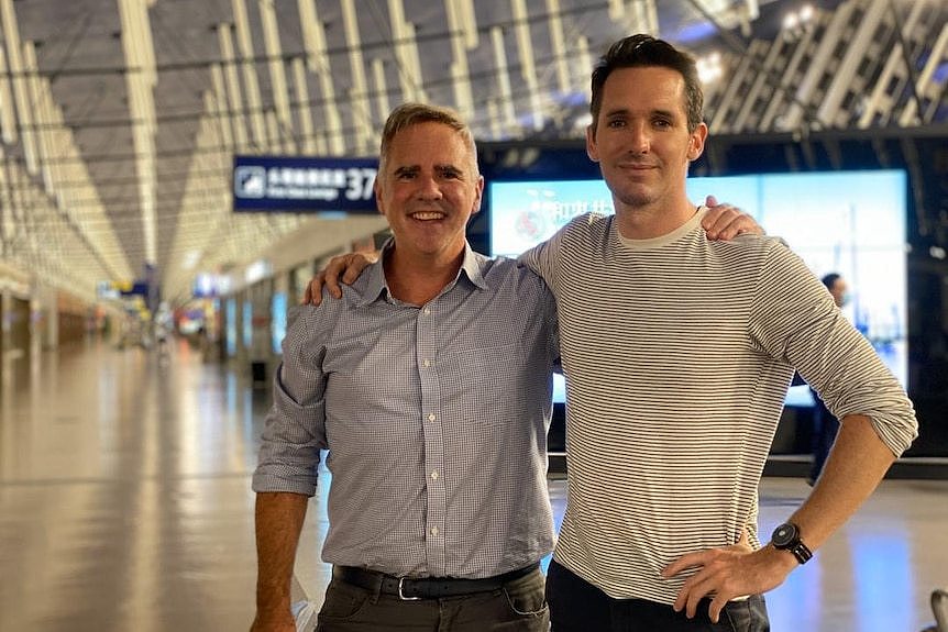 Smith and Birtles with their arms around each others shoulders, as they stand in the middle of Shanghai Airport's terminal