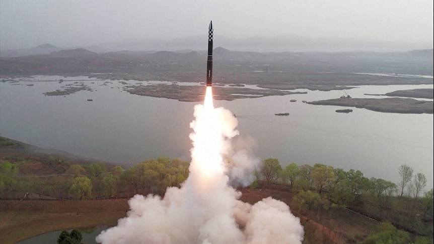 A view of smoke and fire coming from a missle launching in front of a body of water.