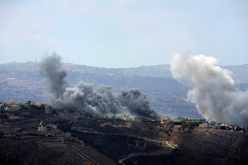 A villages sitting on a ridge is engulfed in grey smoke from air strikes