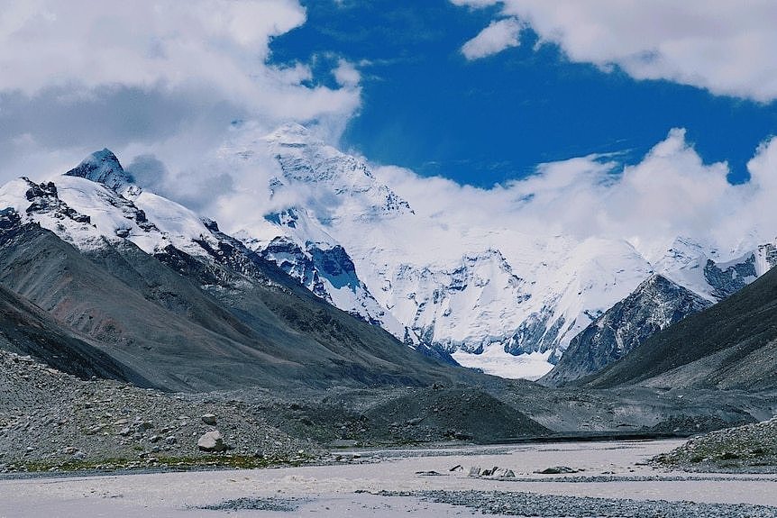 A blue sky, many mountain peaks and a river in the foreground, 