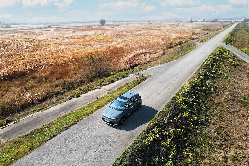 Aerial shot of a grey SUV driving on an unmarked road through vast field of drown and green grass.