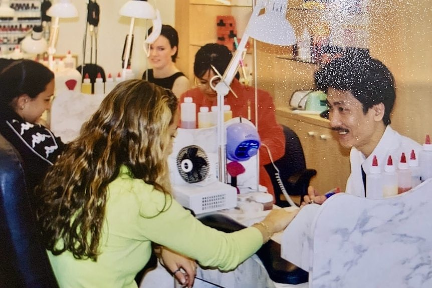 A man smiles as he does a woman's nails in a nail salon.