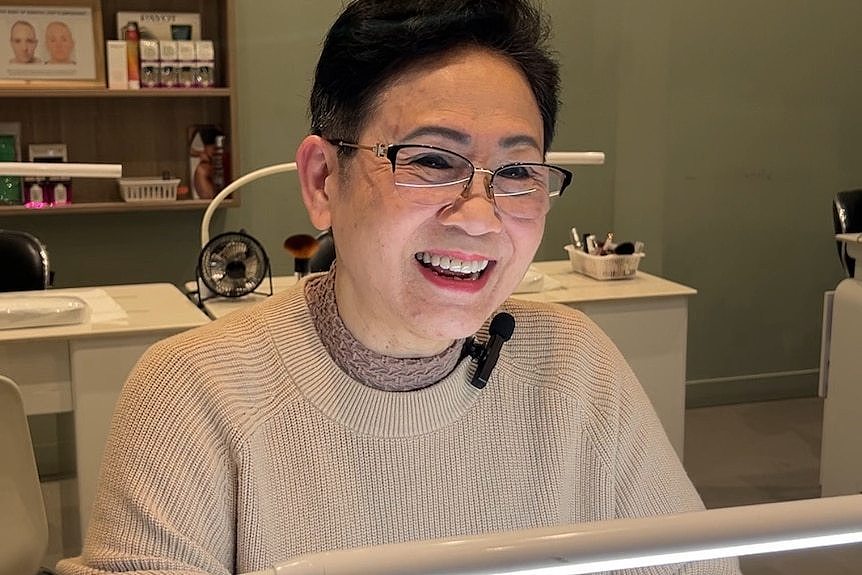 A older woman sits in a nail salon chair preparing to do nails.