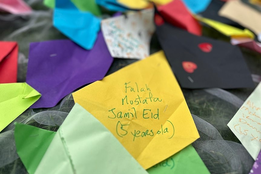 A child's name on a yellow piece of paper in a paper kite memorial outside the State Library of Victoria.