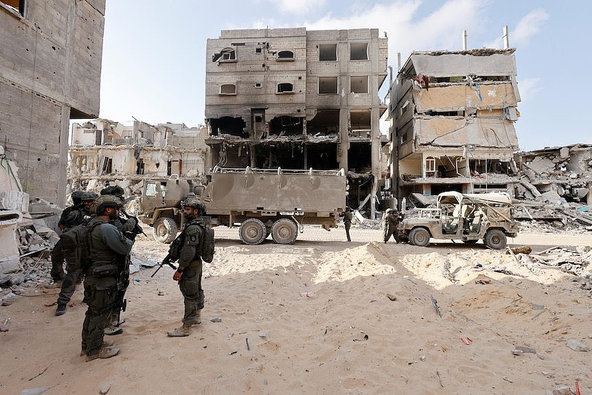 A group of men in combat gear stand in rubble 