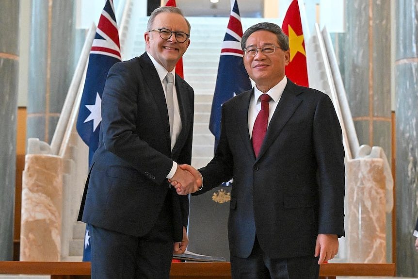 Anthony Albanese wears a dark suit, smiles, and shakes hands with Li Qiang who is in a black suit