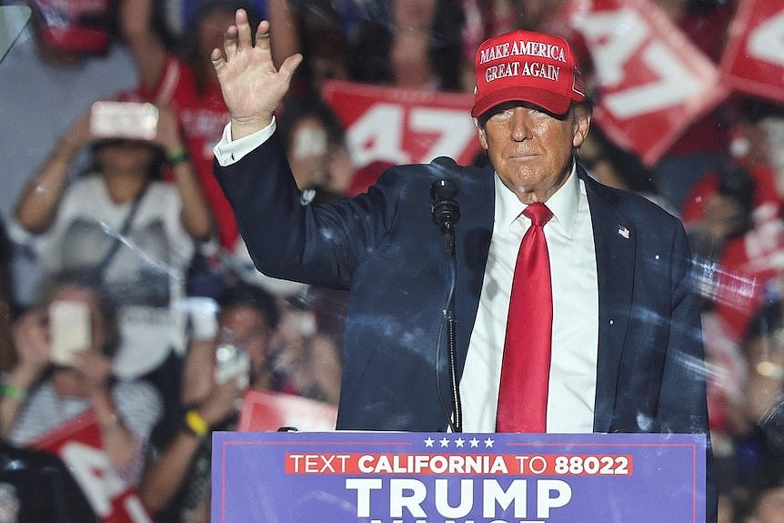 Donald Trump waves to a crowd wearing a red Make America Great Again hat.