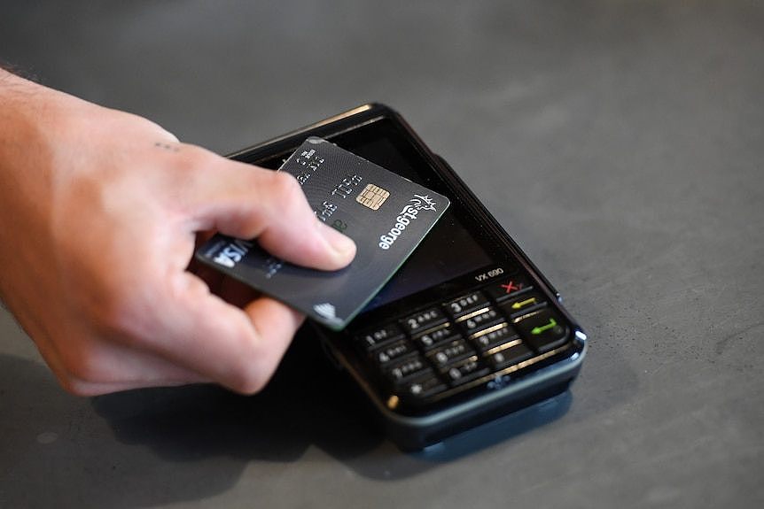 A person holds a grey Visa card next to a black EFTPOS payment terminal