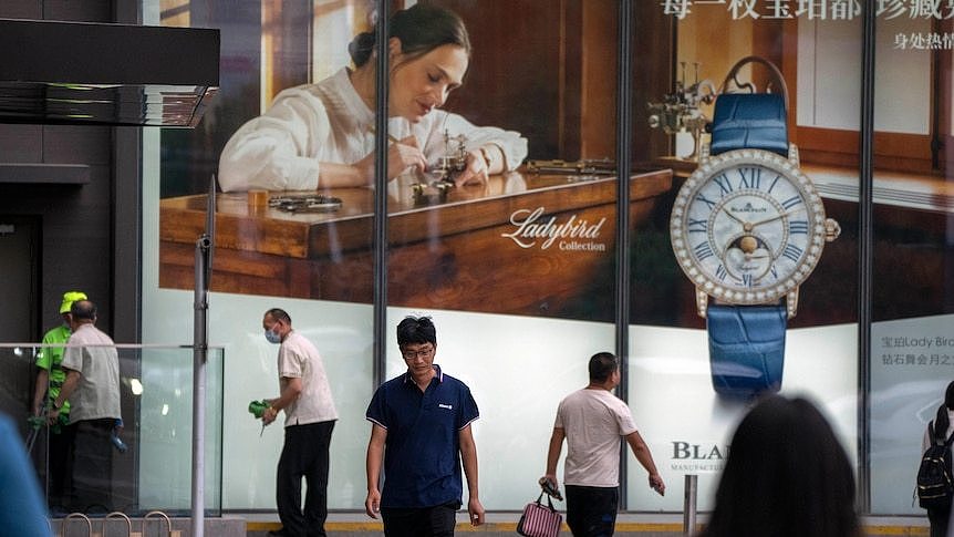 Shoppers walk under a Catier watch advertisement.