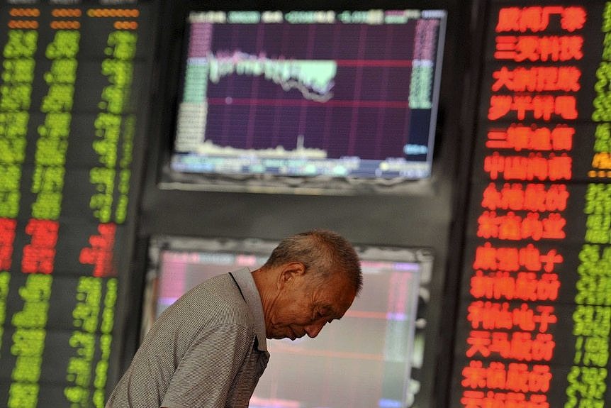 Investor looks down in front of electronic board showing stock information