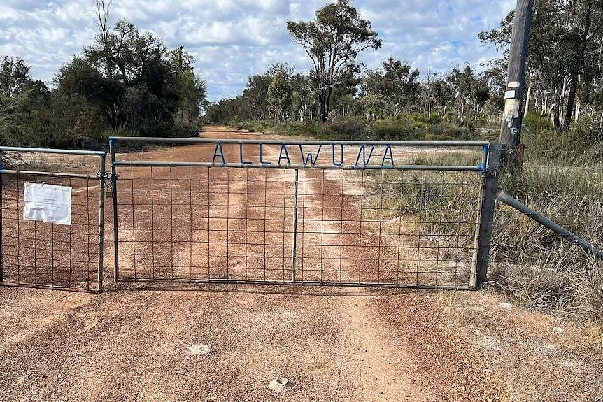 A locked gate with the property name Alllawuna incorporated into the frame and a gravel driveway into bush land 