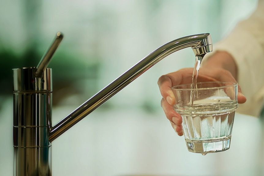 a close-up of a person holding a glass under a running tap, filling it with water