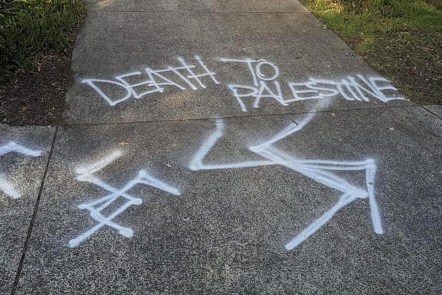 Death to Palestine and swastikas are spray painted on a grey driveway.