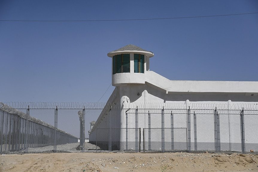 A watchtower sits above a large metal fence with barbed wire