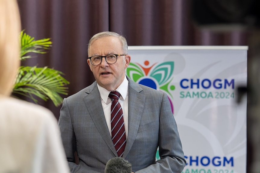 A man in glasses stands in front of a CHOGM sign 