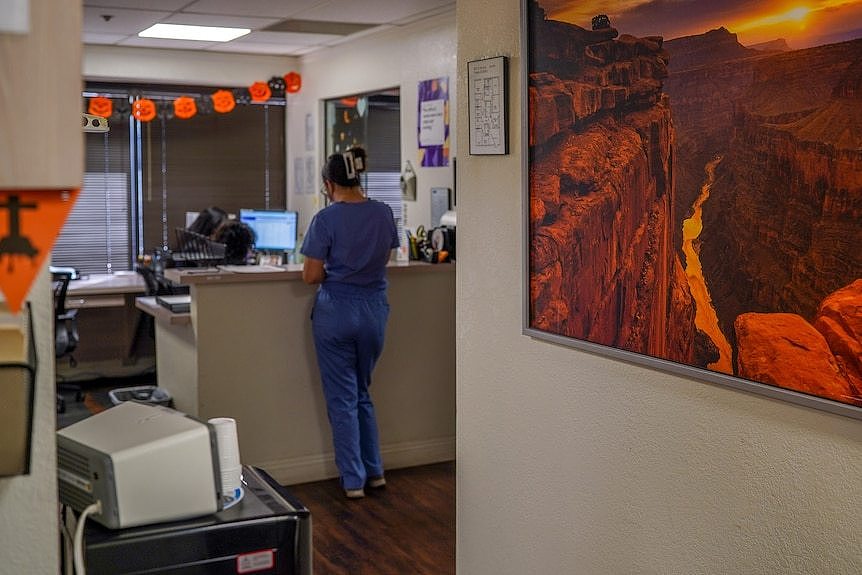 Three medical chairs sit on one side of a room. A desk and chair are on the other. Lanscape pictures are on the wall.