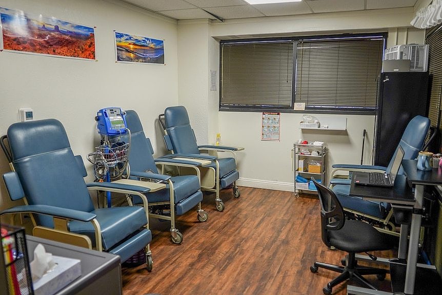 Three medical chairs sit on one side of a room. A desk and chair are on the other. Lanscape pictures are on the wall.