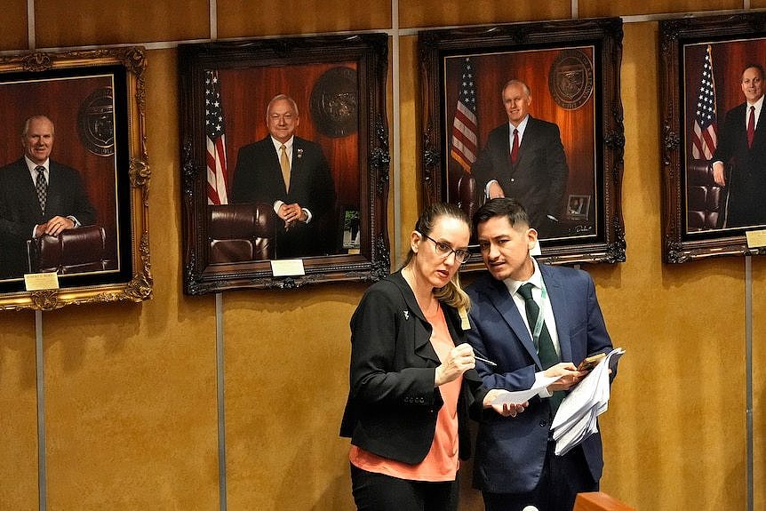 A man and a woman chatting in front of a row of photos of men in suits 