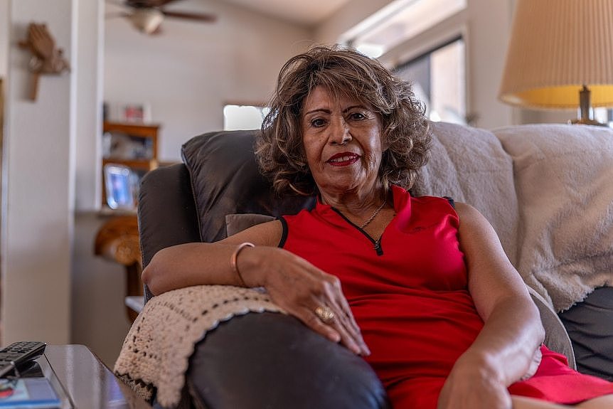 Cristina Junge sits in a leather couch in a house. She wears a red golf dress.