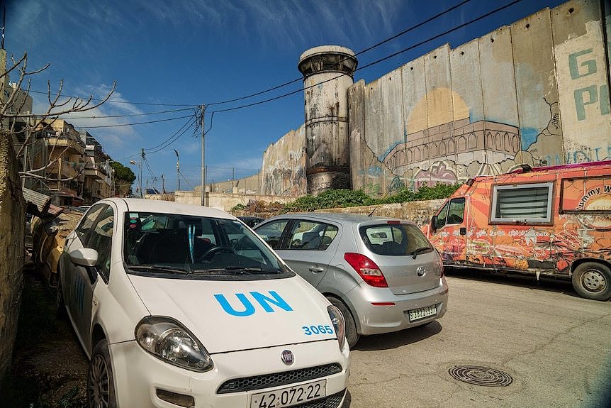 A car with UN on the bonnet is parked near a guard tower on a wall