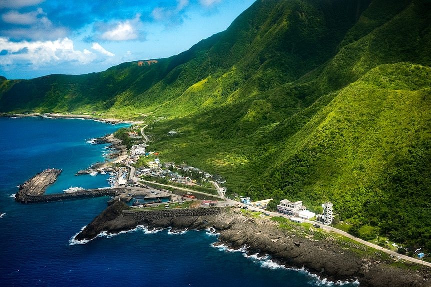 The side of an island with green mountains and blue water 