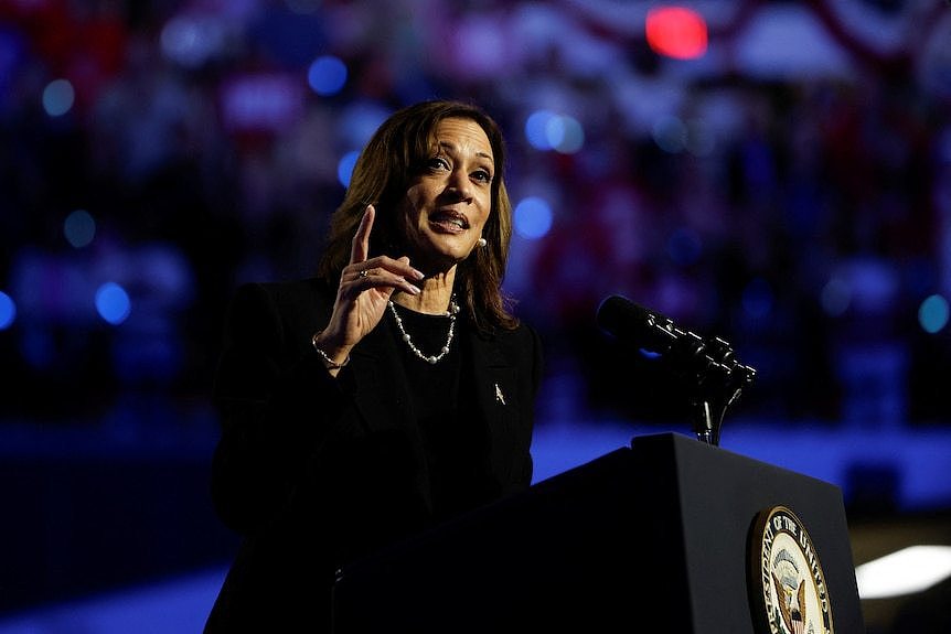 Kamala Harris stands in a black suit with a deep blue backdrop