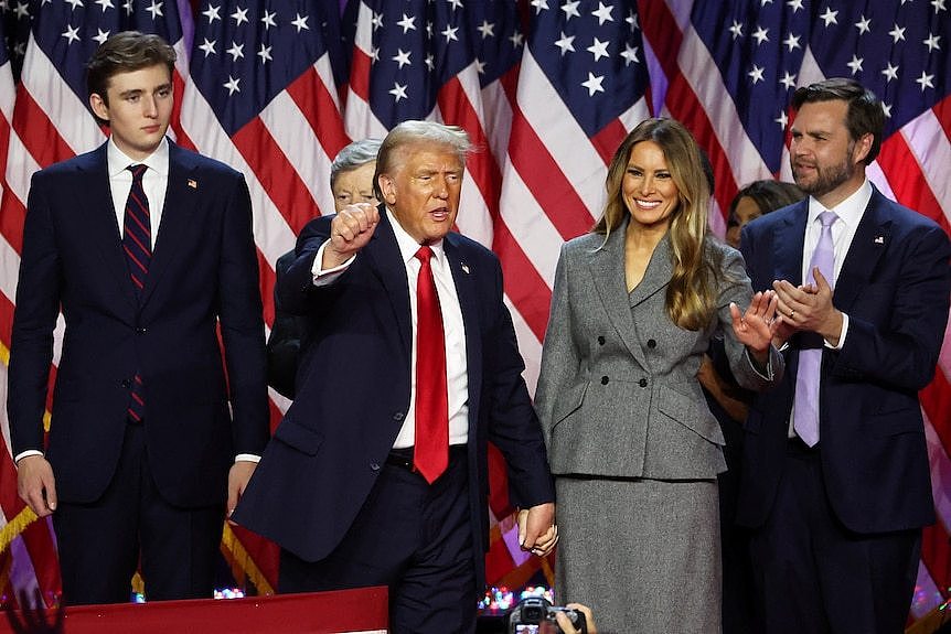 Donald Trump pumps his fist in front of an American flag alongside his family.