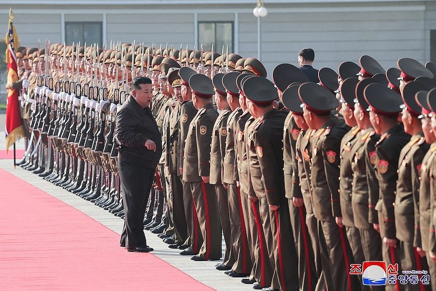 Kim Jong Un in a black suit standing in front of a line of dozens of North Korean soldiers wearing brown