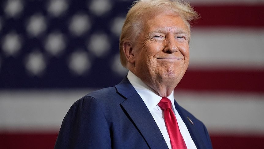 Donald Trump smiles as he stands in front of an American flag.