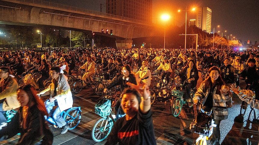 People smiling and waving at camera from their bikes.