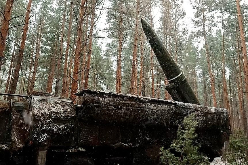 A dark and pointed ballistic missile pointing skyward on a backdrop of forestry