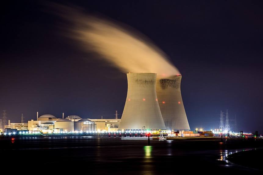 A long exposure shows a nuclear plant illuminated at night, with a white cloud of steam emerging from the top of two reactors. 