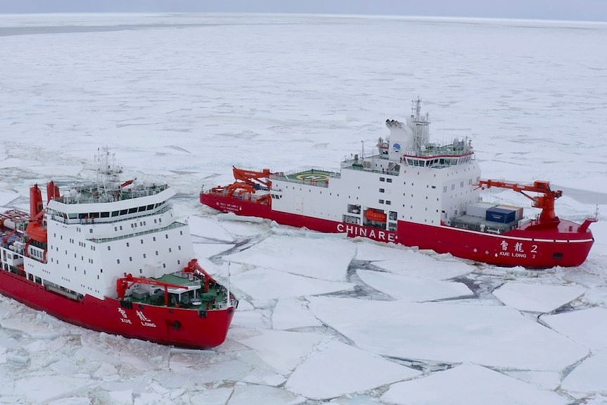 Two red and white ships break through an icy body of water.