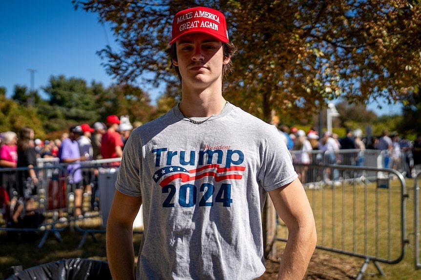 Jack Lawrence, wearing a grey 'Trump 2024' t-shirt and red 'Make America Great Again' cap, stands near a queue of people outside