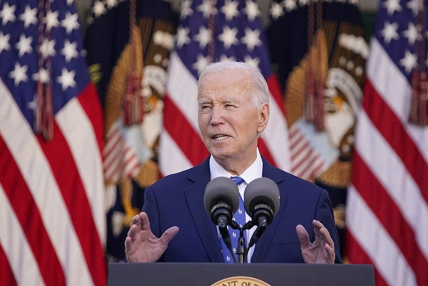 Joe BIden speaks at podium in suit with US flags behind him