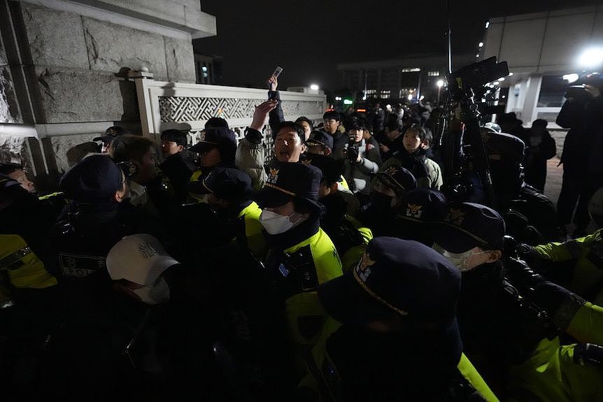 Police holding a line out the front of a parliament building as people try to push their way through