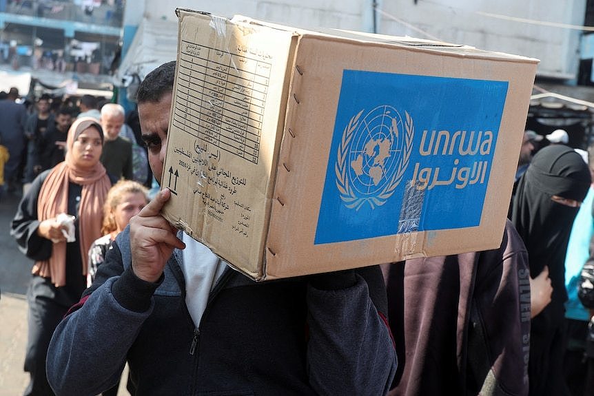 A man carries a blue and beige box with Arabic writing.