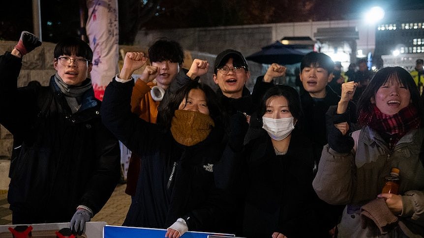 A group of four people chant and waive their fists in the air in protest at night