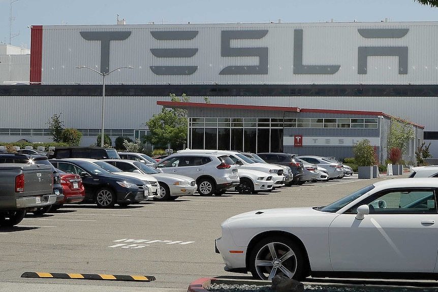 A parking lot outside a large warehouse building with TESLA signs