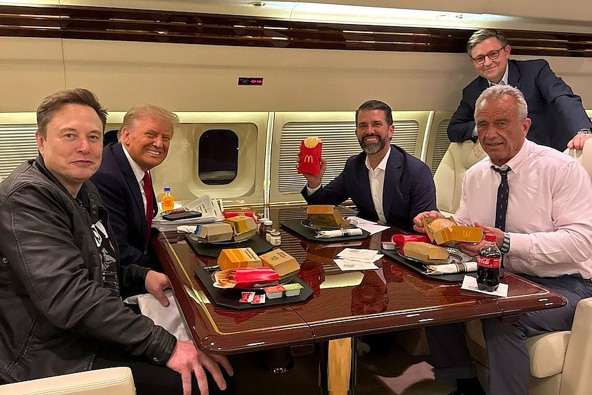 lon Musk, Donald Trump, Donald Trump Jr and RFK Jr sit around a table on a plane with McDonalds in front of them.