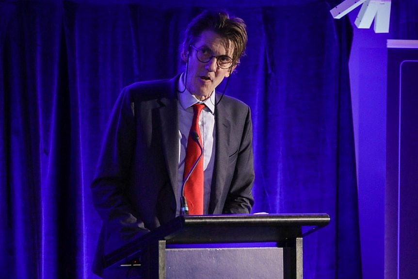 A man in a suit speaking at a lectern. 