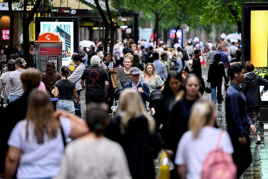 A crowd of people walking along a street carrying shopping bags on an overcast day.