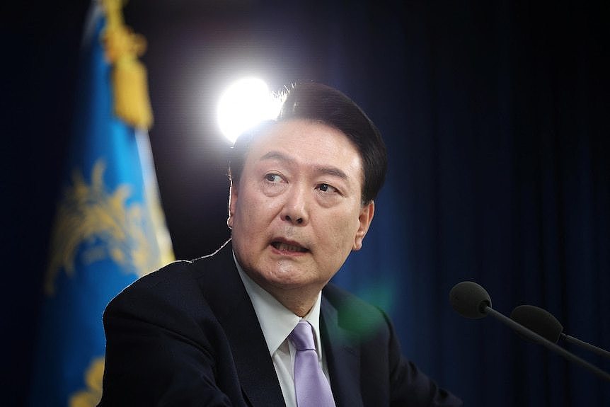 A man in a suit with black hair looking solemn 